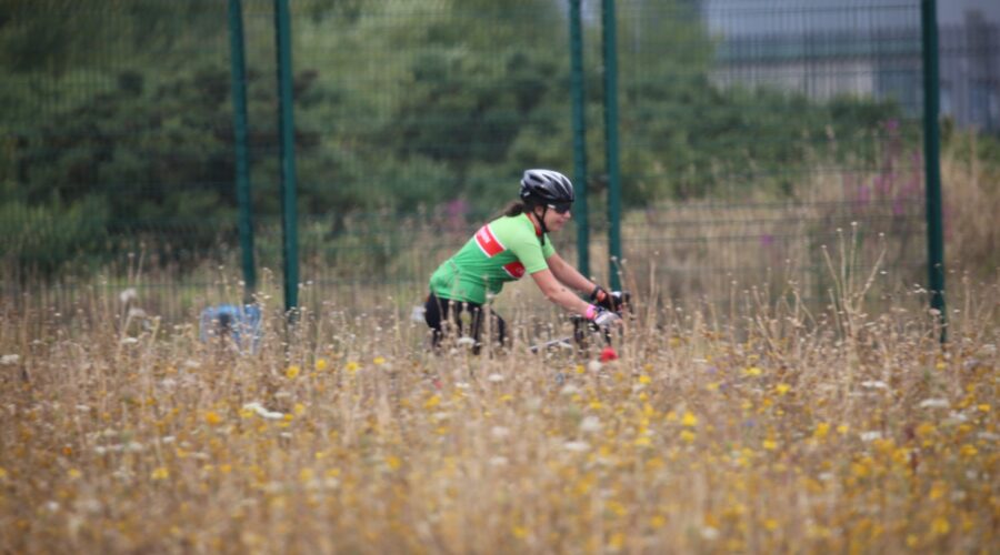 View of a woman cycling her bike behind high grass.