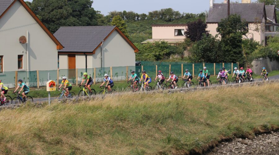 Side line view of group of people cycling along stretch of road.