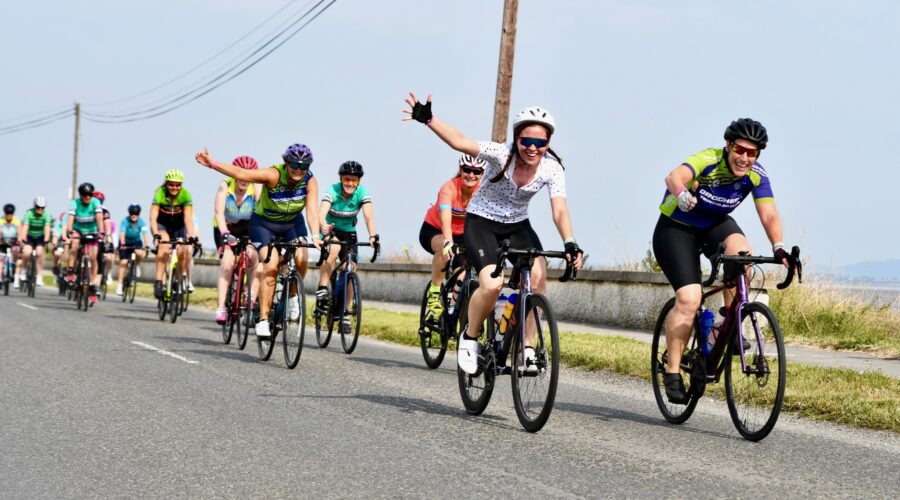 Women on bikes wave as they cycle past.