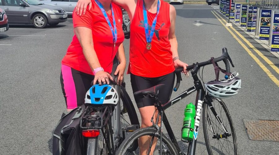 Two women in red shirts stand next to their bikes.