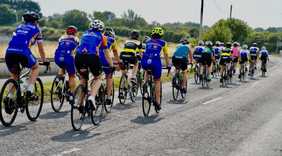 Group of women cycle along stretch of road.