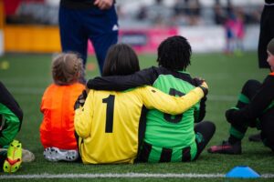 Young soccer players have arms around each other on pitch.