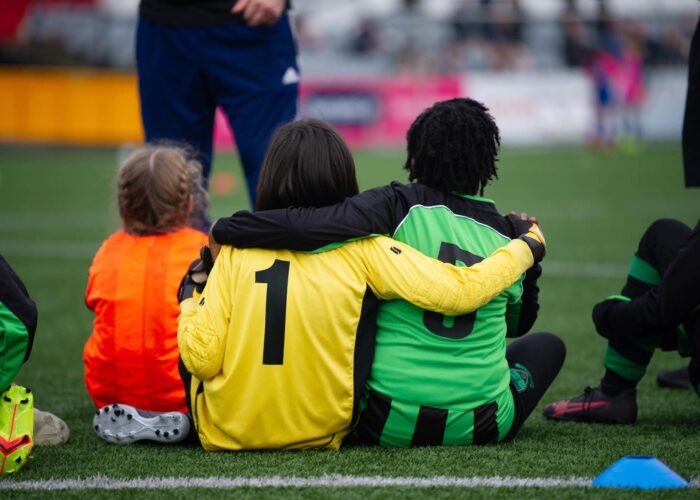 Young soccer players have arms around each other on pitch.