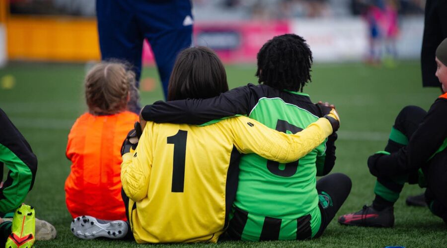 Young soccer players have arms around each other on pitch.