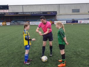 Referee talks with two young girls on soccer pitch.