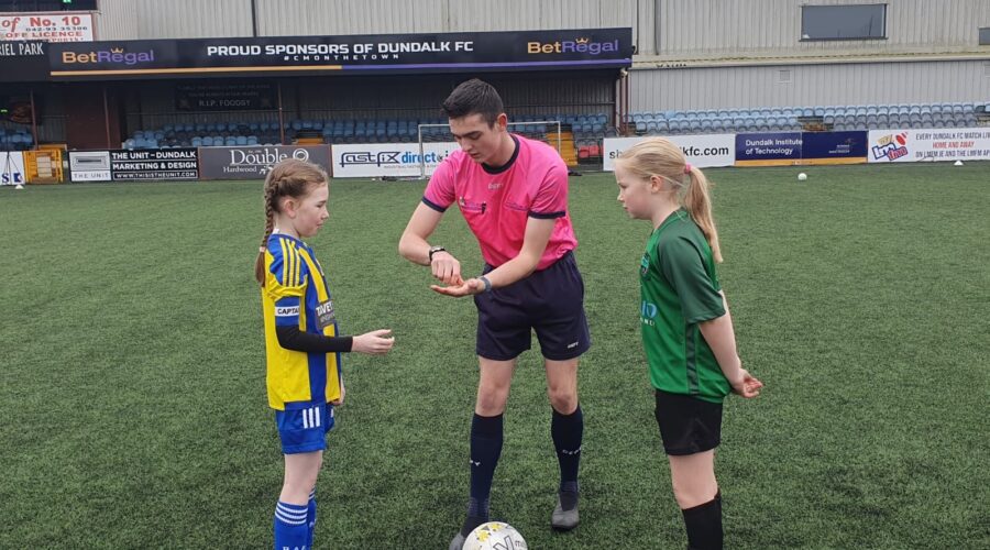 Referee talks with two young girls on soccer pitch.
