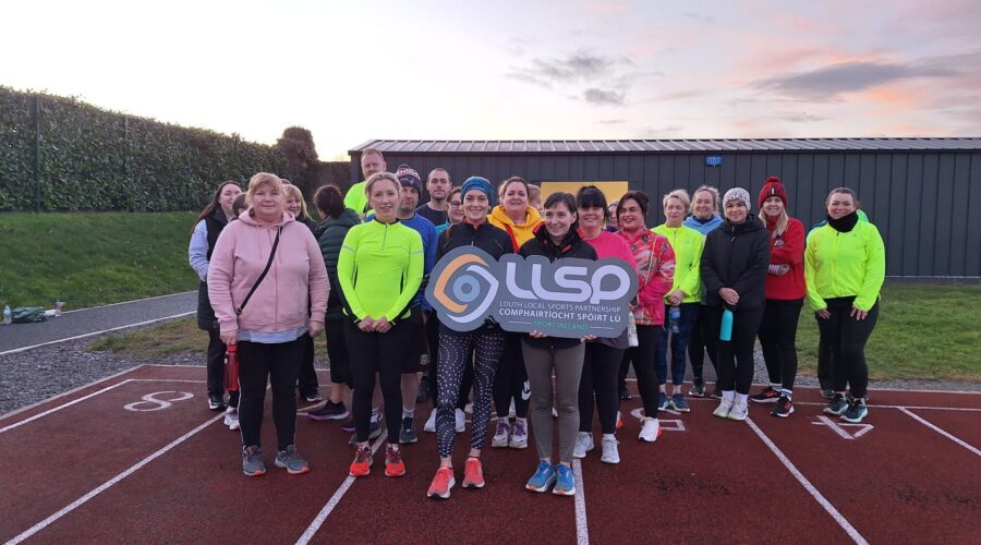 Moneymore Hub - Group of people holding LLSP sign on running track.