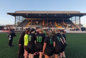 Group of young girls huddle on soccer pitch.