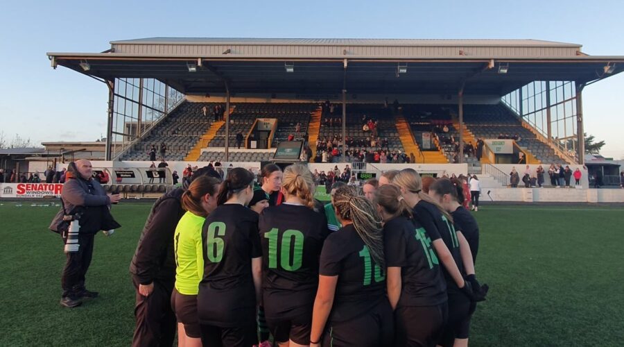 Group of young girls huddle on soccer pitch.