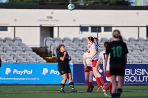 Young girls play soccer on pitch.