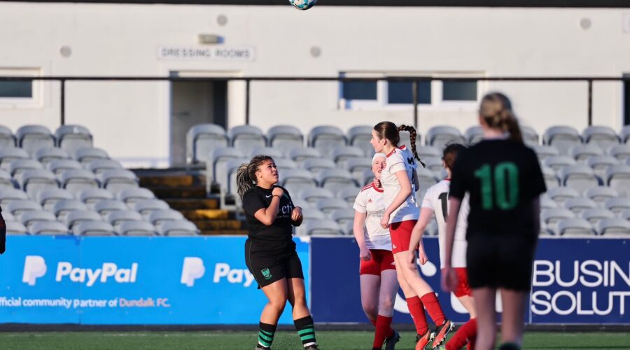 Young girls play soccer on pitch.