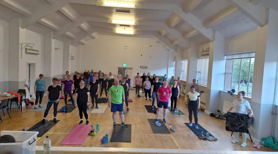 Moneymore Hub - Bootcamp of people standing by yoga mats in a wooden floored hall.