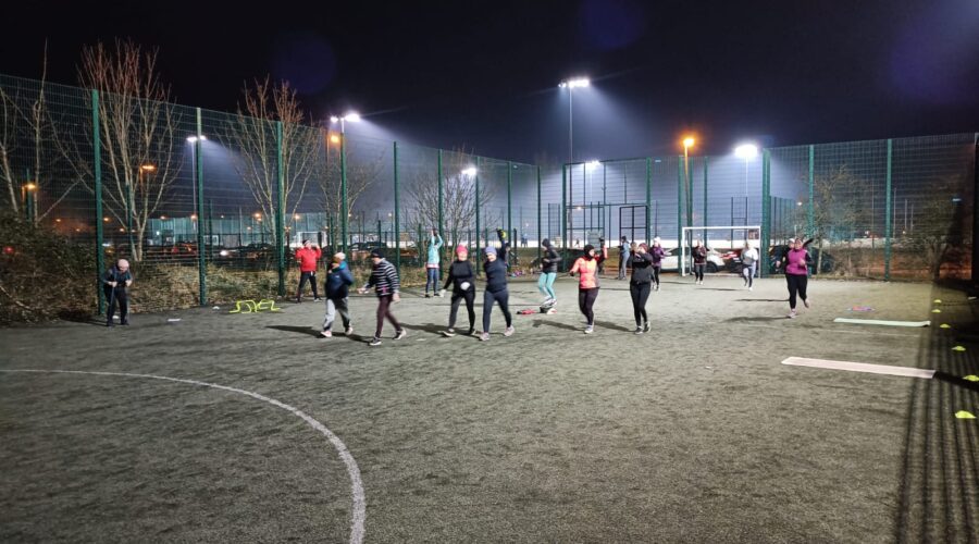 Muirhevnamor Hub - Group of people stay active on a frosty pitch at night.