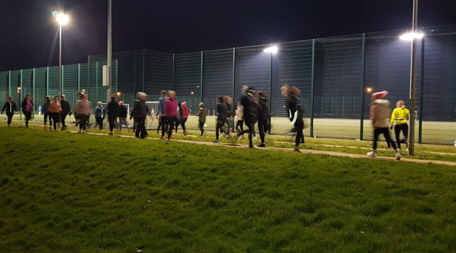 Muirhevnamor Hub - Couch to 5K group of people run along path at night.