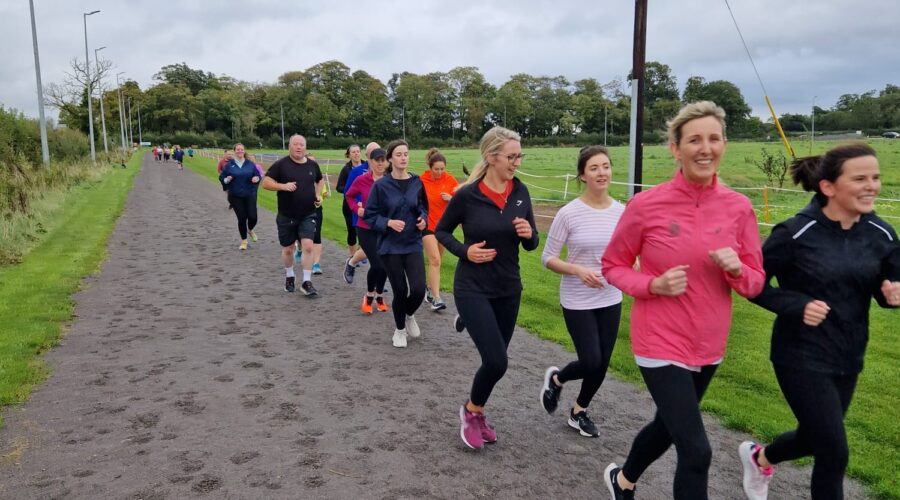 Moneymore Hub - Group of women smile while power walking on a dirt track.