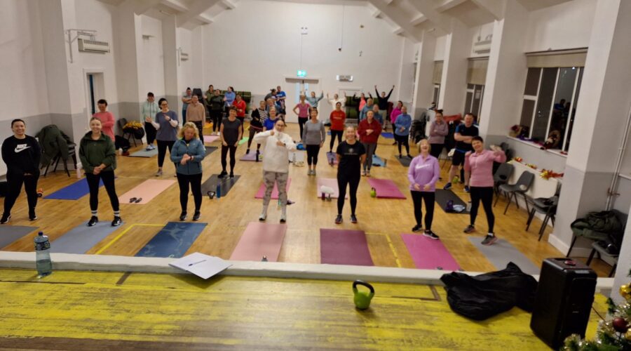 Moneymore Hub - Bootcamp of people standing by yoga mats in a wooden floored hall.