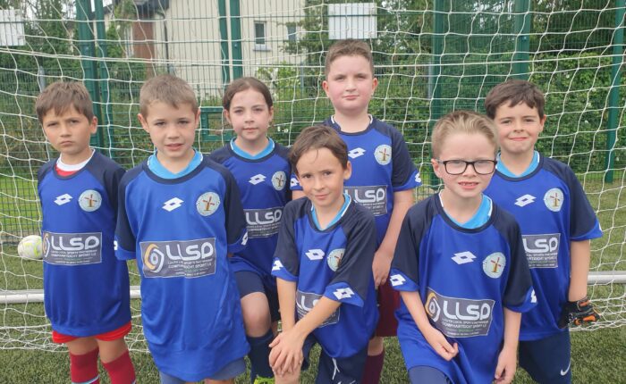 Young boys pose in LLSP sports jerseys under soccer net.