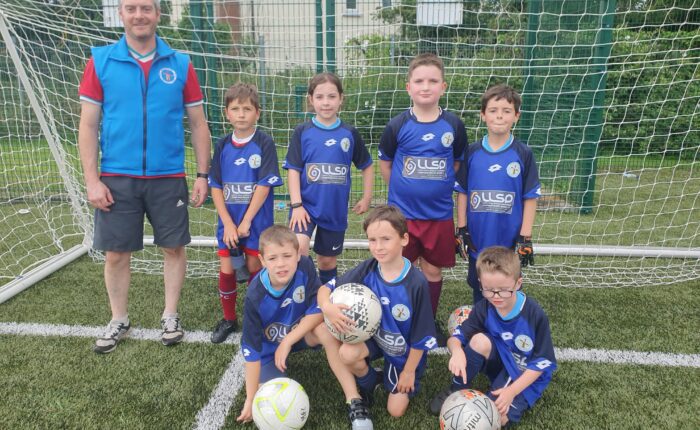 Young boys and coach pose in sports jerseys under soccer net.