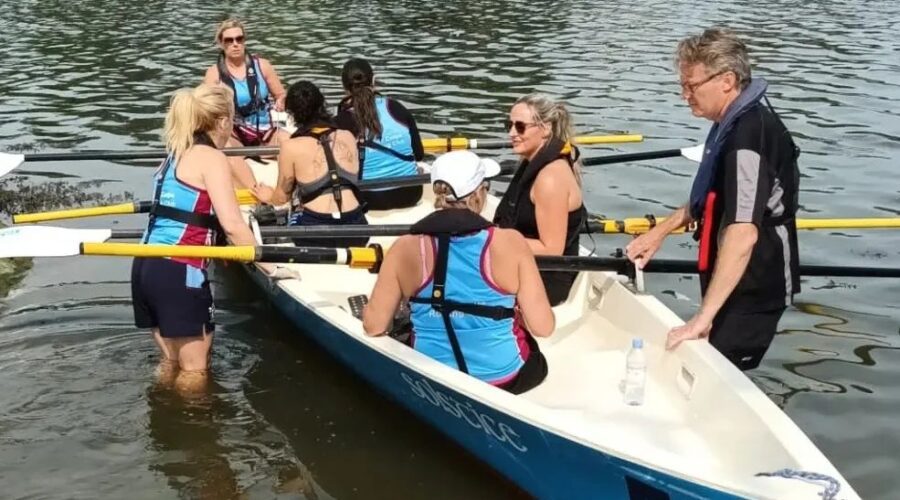 Group of people sit in a rowing boat on water.
