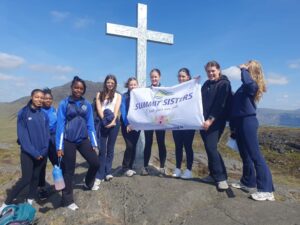 Group of girls hold sign that reads, 'Summit Sisters' while next to a large cross.