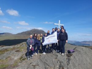 Group of girls hold sign that reads, 'Summit Sisters' while next to a large cross.