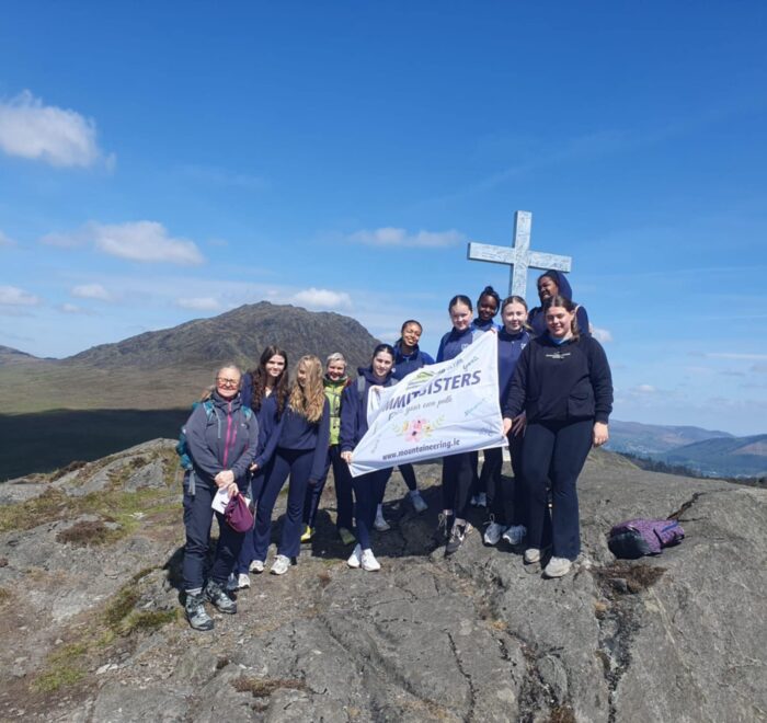 Group of girls hold sign that reads, 'Summit Sisters' while next to a large cross.