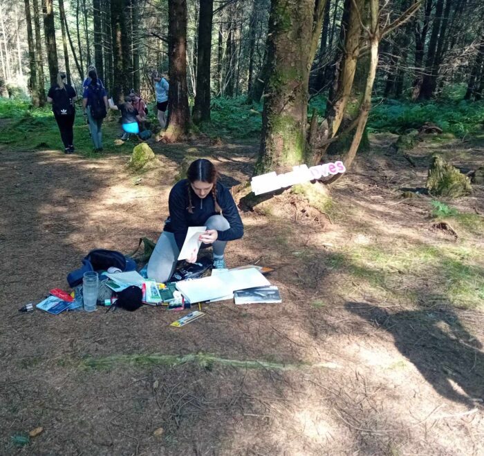 Young girl kneels on ground in forest and checks paper.