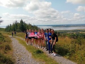 Group of girls hold sign for Her Moves along forest path.