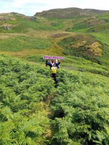 Girl hold up sign for Her Moves above head with back turned to camera in a field of green grass.