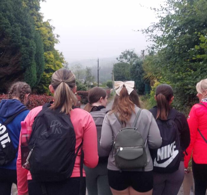 Group of girls walk along road with backs turned to camera.