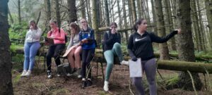 Group of girls sit on fallen tree trunk in forest.