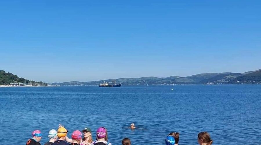 Group of girls stand at waters edge and listen to instructor.