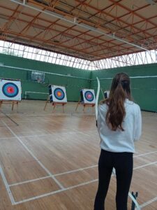 Teenage girl plays archery with back turned to camera.