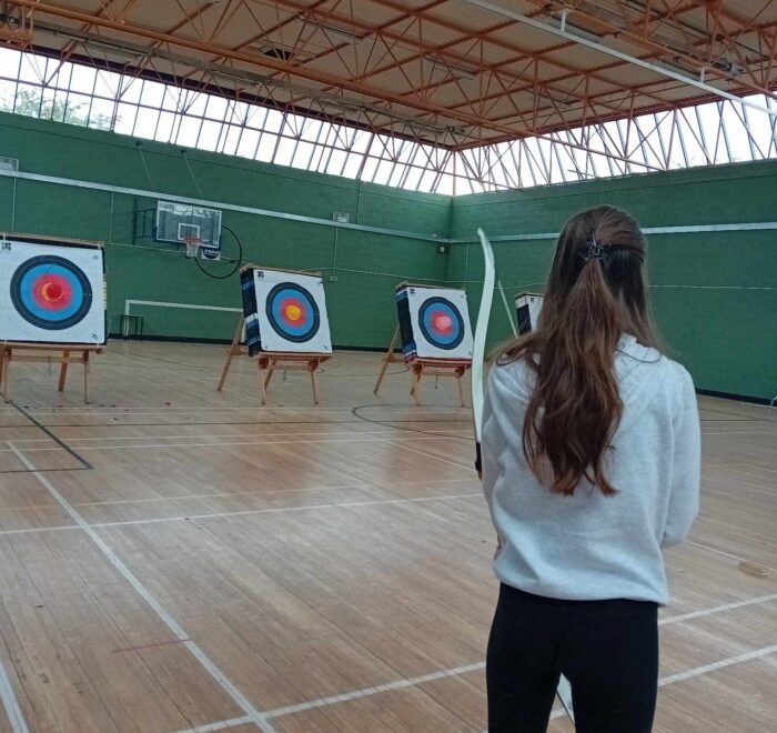 Teenage girl plays archery with back turned to camera.