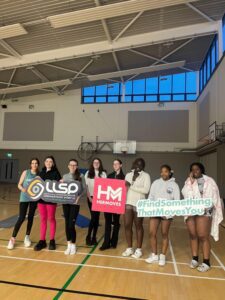 Group of girls hold signage for Her Moves in gym.