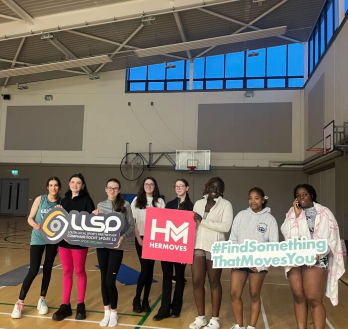 Group of girls hold signage for Her Moves in gym.