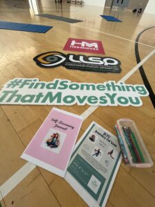 Signage for Her Moves is laid out on floor of gym.