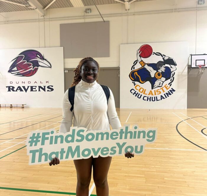 Girl holds sign that says #FindSomethingThatMovesYou while in gym.
