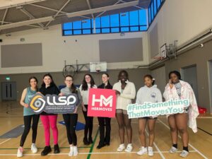 Group of girls hold signage for Her Moves in gym.