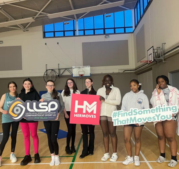 Group of girls hold signage for Her Moves in gym.
