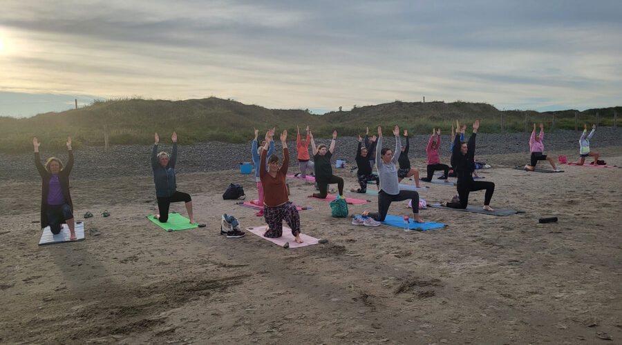 Group of women do yoga on beach in the evening time.
