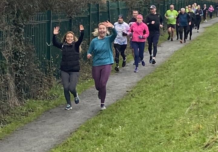Muirhevnamor Hub - Group of people run along dirt path and wave at camera.