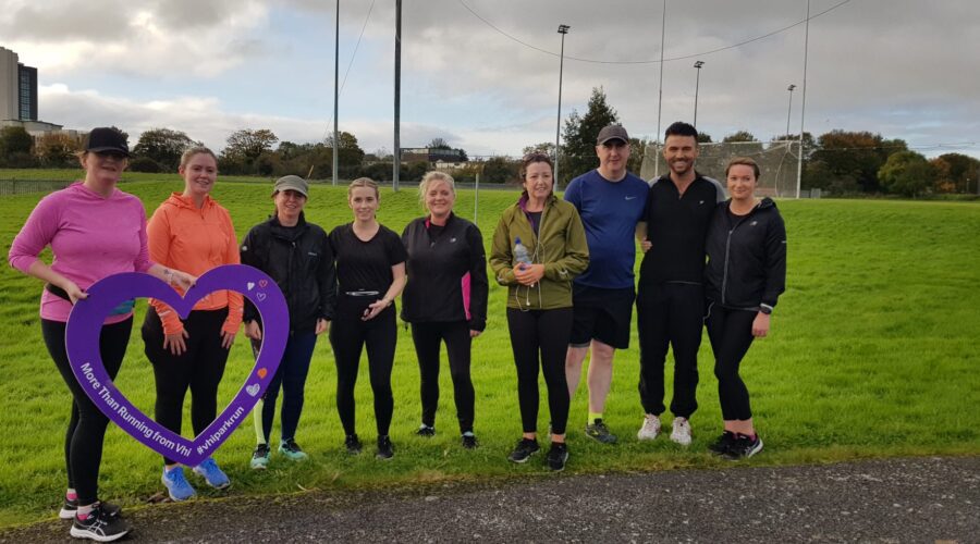 Muirhevnamor Hub - Group of people pose near field holding a heart-shaped cut-out that says 'More than Running from VHI'.
