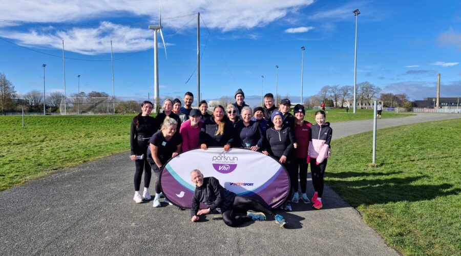 Muirhevnamor Hub - Couch to 5K group of people pose by signage for VHI's Parkrun.