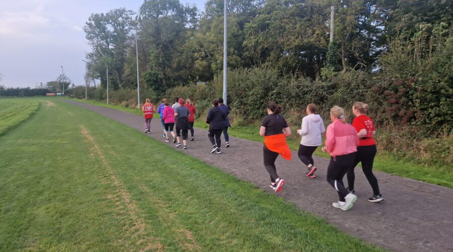 Moneymore Hub - Group of women smile while power walking on a dirt track.