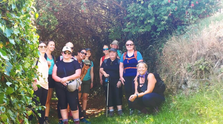 Group of women smile for picture surrounded by greenery while hiking.