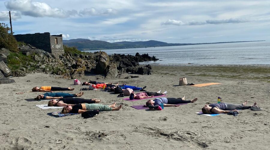 Group of women lie on yoga mats on sand at beach.