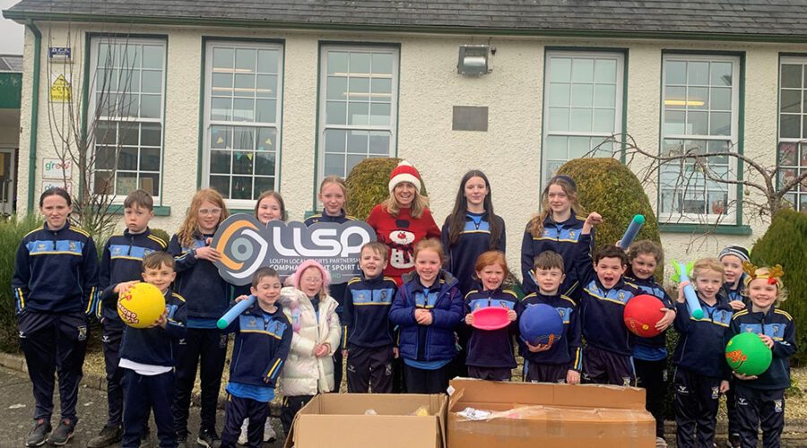 Young children hold sports equipment in front of school.
