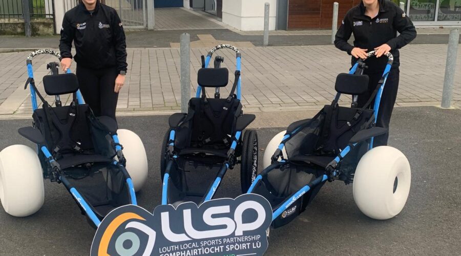 Two women stand next to beach buggies and a sign for LLSP.