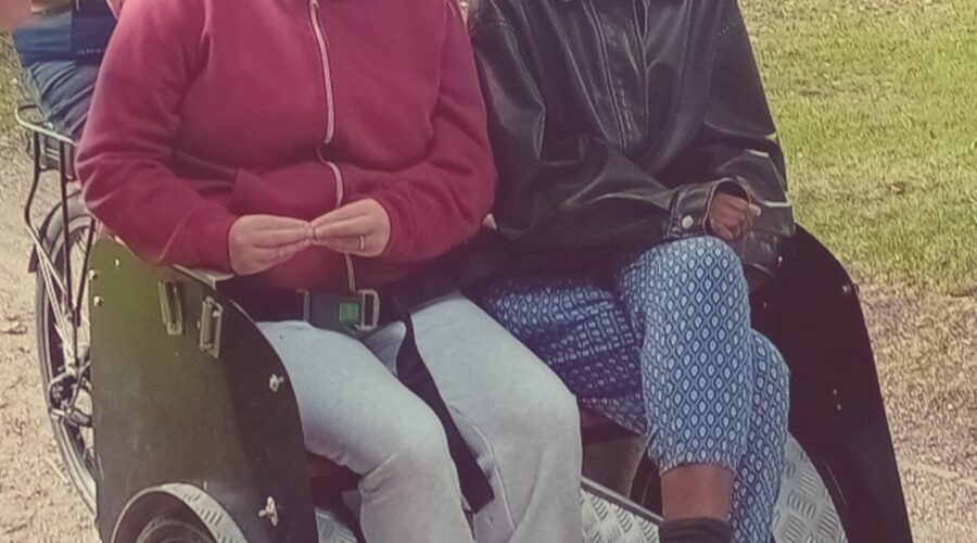 Two women on a push bike cycle through park for Come n' try in the park.